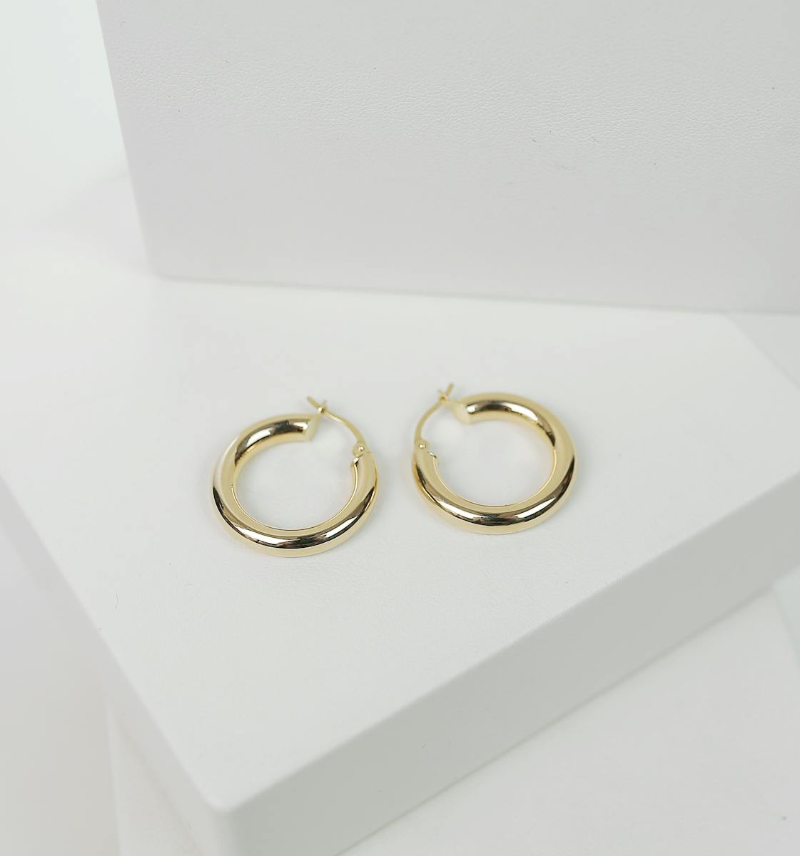 Chic gold hoop earrings displayed on a minimalist white surface, perfect for fashion collections.