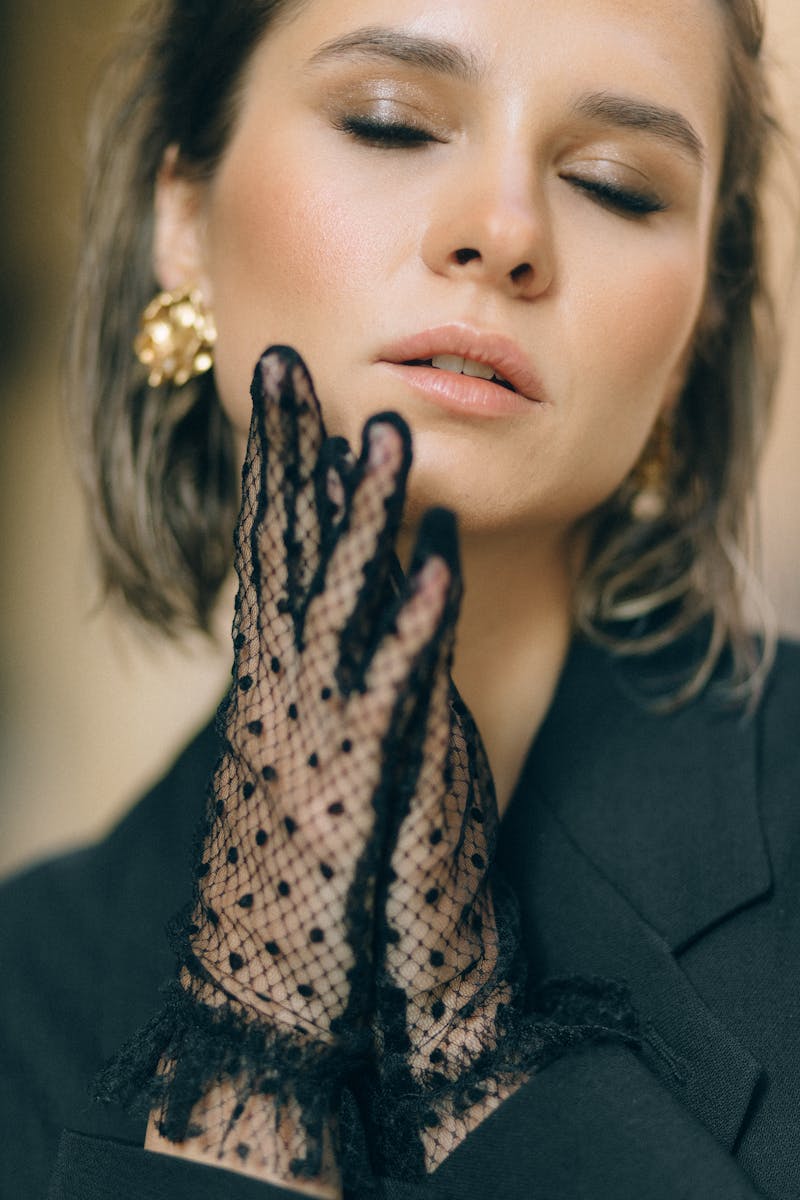 Close-up portrait of a woman wearing fashionable lace gloves and gold earrings.