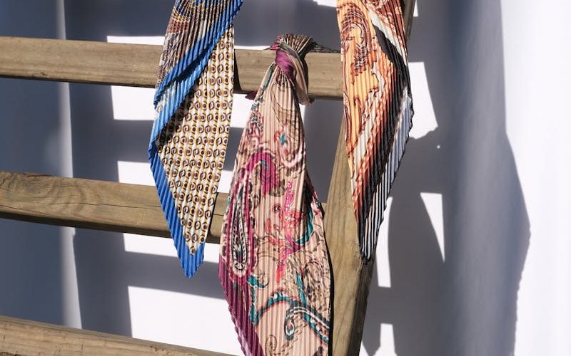 Three vibrant silk scarves tied to a wooden ladder casting shadows on a wall.